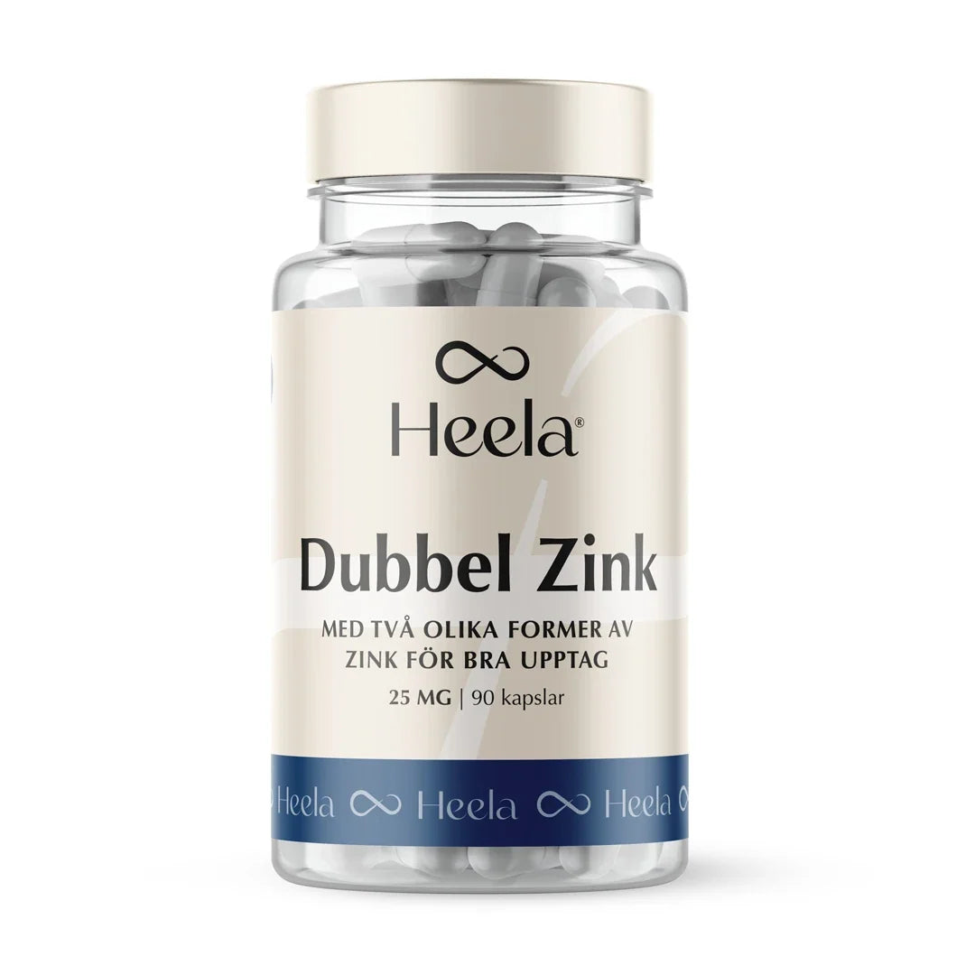 Heela Dubbel Zink 60 caps i en transparent burk med vita kapslar, beigefärgad etikett och blå bottenrand.